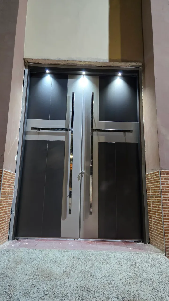 Puerta de ACM de doble hoja de noche, con luces empotradas sobre muro de ladrillo visto