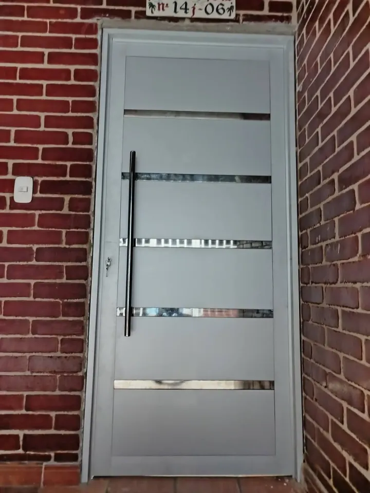 Puerta de ACM gris con ranuras horizontales sobre muro de ladrillo visto