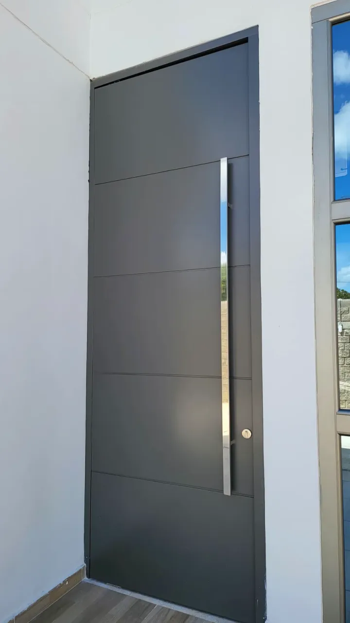 Puerta de ACM gris oscuro con tirador vertical de acero, sobre suelo de madera