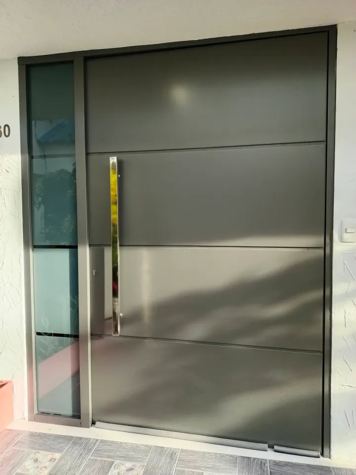 Puerta de ACM gris de gran formato con paños de vidrio laterales