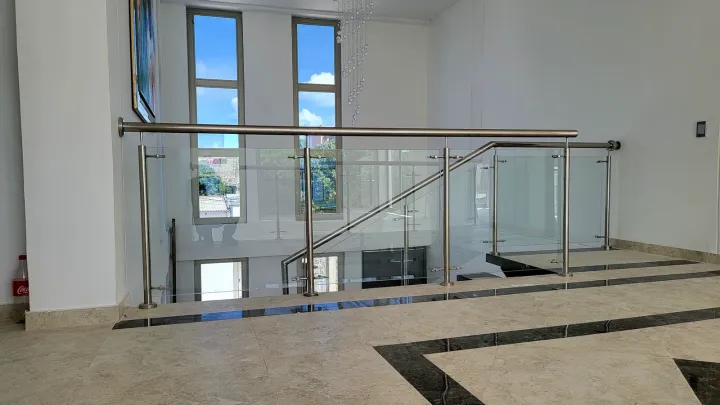 Interior a doble altura con baranda de vidrio y ventanales verticales