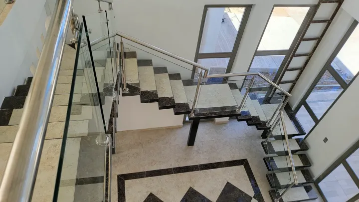 Escalera con baranda de vidrio vista desde arriba, sobre suelo de mármol despiezado
