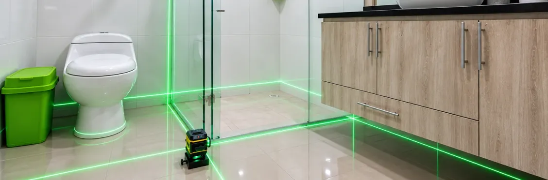 Nivel láser de líneas verdes en el suelo de un baño, proyectando sus líneas sobre el piso y la división de vidrio de la ducha