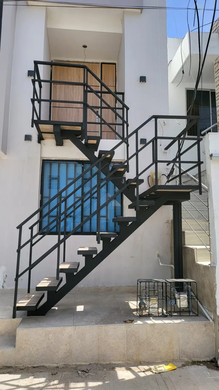Escalera metálica negra exterior contra fachada blanca y ventana azul